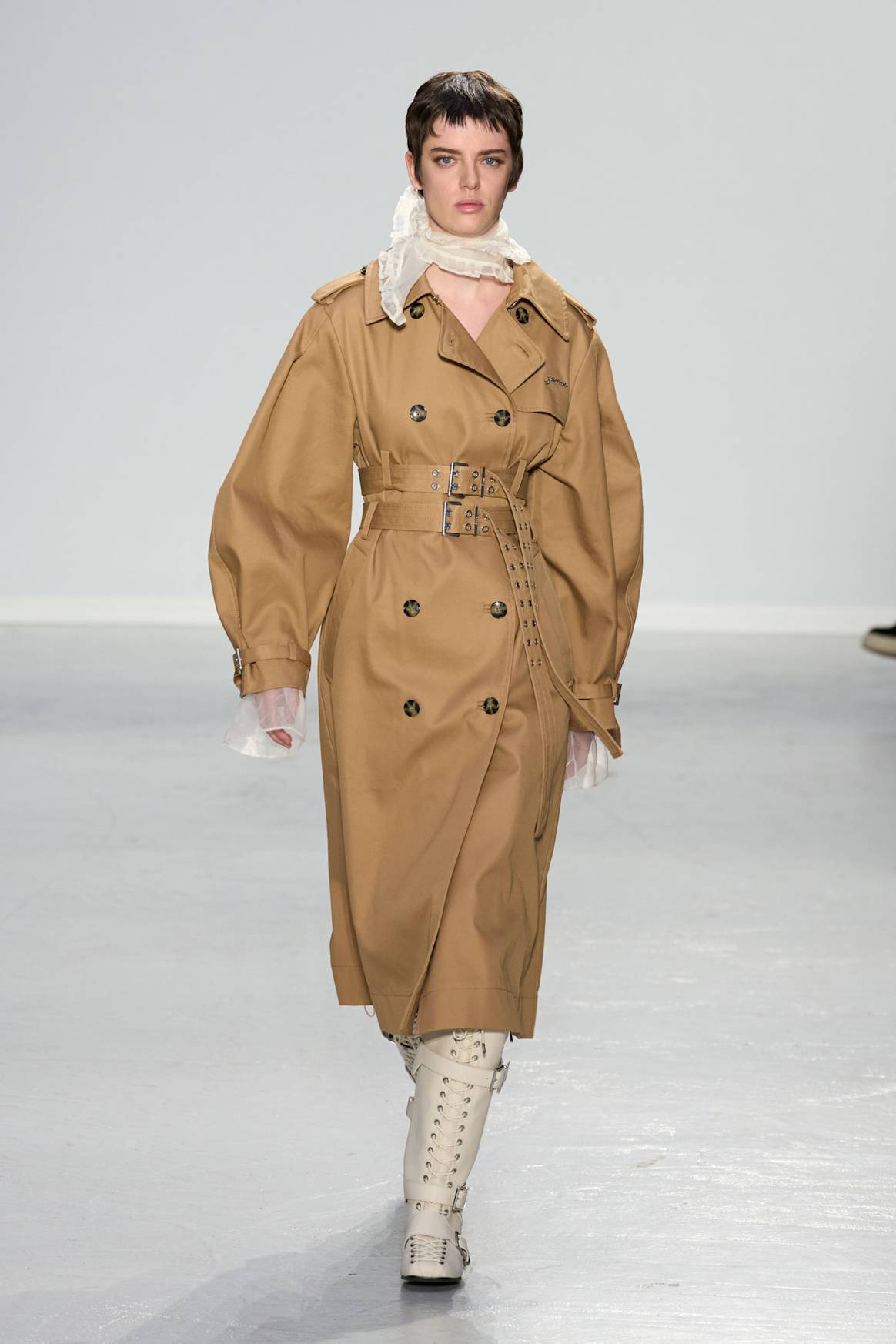 Look 2: Een lange beige trenchcoat met lichte sjaal en veterlaarzen