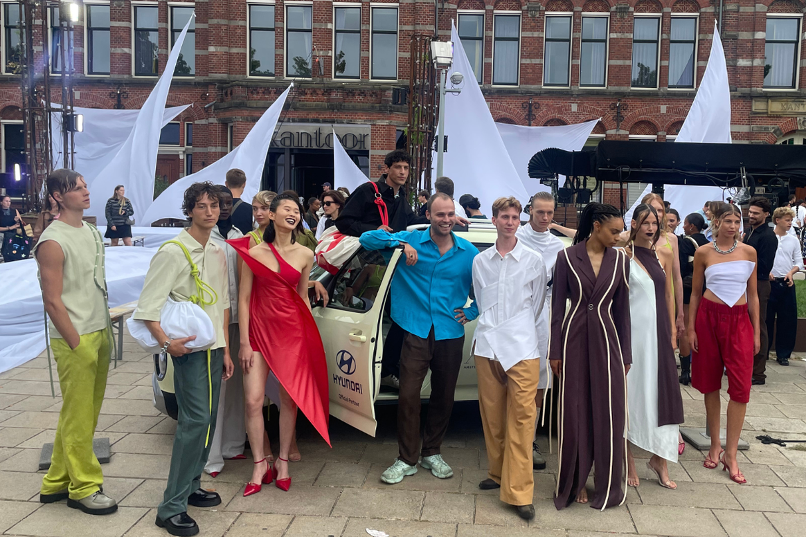 Douwe de Boer y Diek Pothoven frente a un auto eléctrico Hyundai rodeados de los modelos del desfile