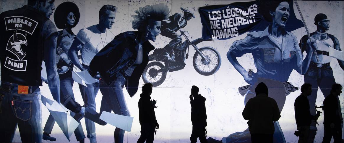 El motociclista, el niño flor, el rebelde, el punk, el vaquero, la sufragista, el líder de los derechos civiles, todos vestían jeans. La pancarta dice "Las leyendas nunca mueren" y los volantes esparcidos indican el caos del movimiento, todo se lanza por los aires. Imagen: Kristy Sparow