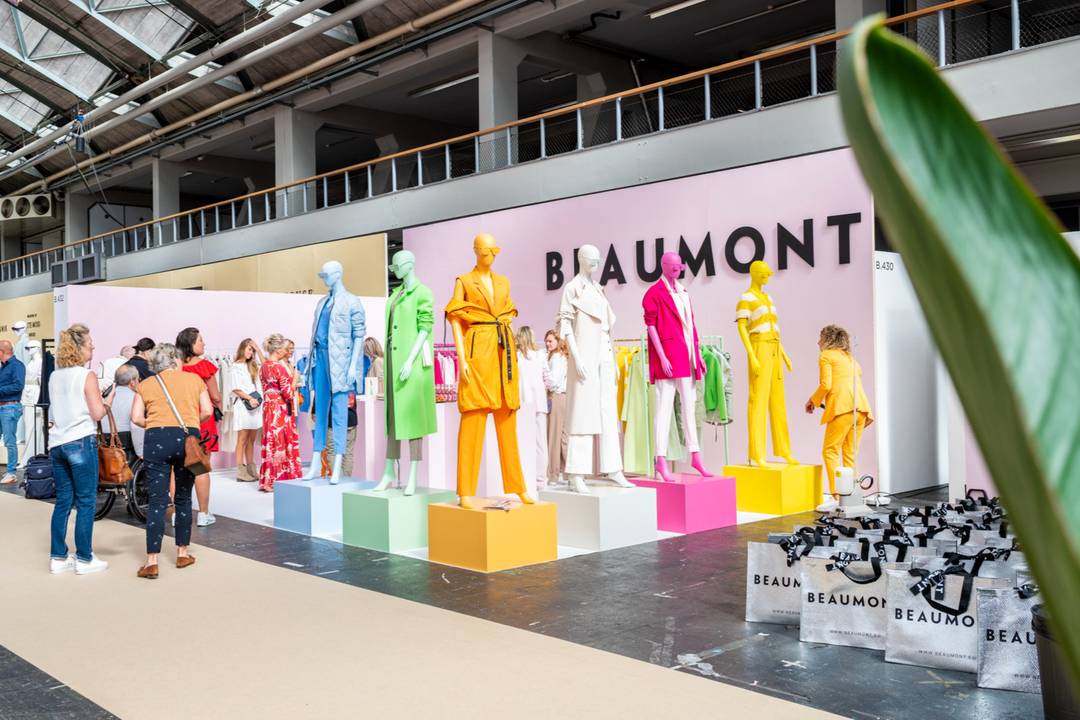 Mannequins in kleurrijke outfits, tentoongesteld op kleurrijke dozen tijdens een modebeurs. De afbeelding illustreert het gebruik van kleur in visuele merchandising.