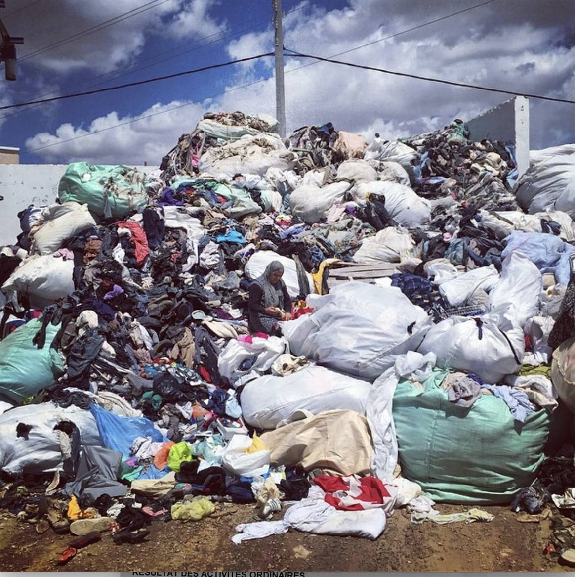 Ein Berg ausrangierter Oxfam-Kleidung in Tunesien mit einer Frau, die die Überreste durchwühlt. Ein klares Beispiel für schlechte Praktiken mit überschüssigen Lagerbeständen, fahrlässiger CSR und mangelndem Fachwissen bei der Lösung sehr realer Probleme.