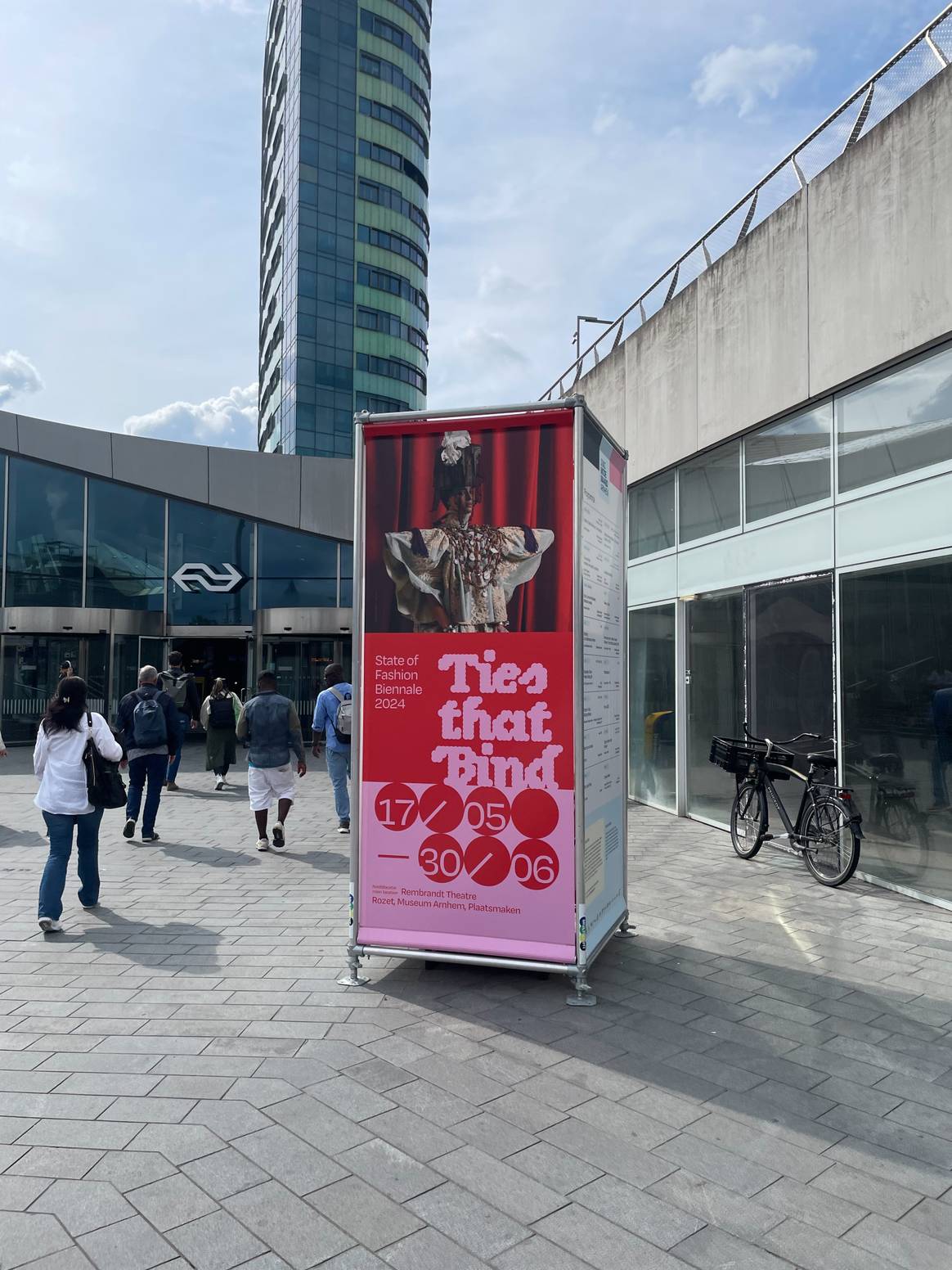 Buiten station Arnhem Centraal staat een groot bord met 'State of Fashion biennale 2024' en het thema 'Ties that Bind'.