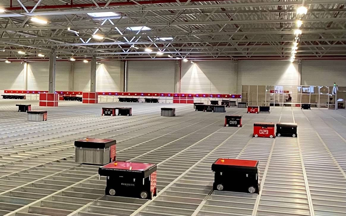 Foto: FashionUnited.de / Die roten Roboter nehmen die Kisten mit der Ware auf und transportieren sie zum Mitarbeiter.
