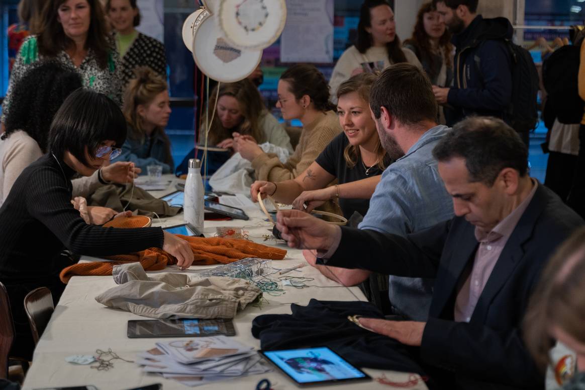 Bezoekers van het festival in Pakhuis de Zwijger, bezig met het repareren van hun kledingstukken. Foto: Tess van der Sluis / Pakhuis de Zwijger